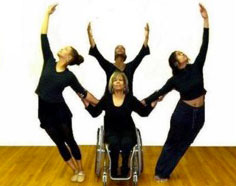 Dance performance with three women raising  their hands and radiating out from a woman using a wheelchair. 